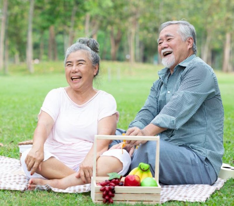 older couple sitting down on a blanket enjoying a picnic in the park